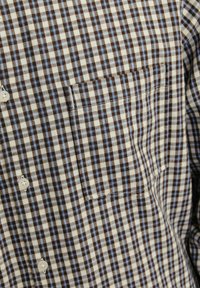 Camisa de botones con un patrón de cuadros en marrón, azul y crema. Presenta un solo bolsillo en el pecho y está hecha de una tela suave y ligera.