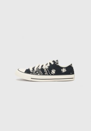 Zwarte canvas sneaker met witte bandana patronen, gebroken witte veters en rubberen zool. Laagtop ontwerp met contrasterende neuskap.