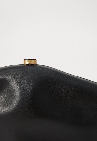 Black leather bag with a smooth texture; features a gold accent with engraved branding at the top. Curved, minimalist design.