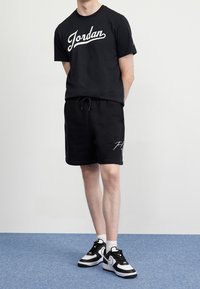 Czarny bawełniany t-shirt z białym logo "Jordan", w połączeniu z czarnymi szortami z polaru z białymi akcentami. Czarno-białe sportowe sneakersy.