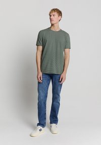 Groene gestreepte t-shirt met korte mouwen, ronde hals, gecombineerd met blauwe jeans en witte sneaker. Eenvoudig, casual ontwerp met een comfortabele pasvorm.