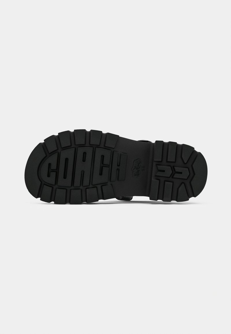 Suela de zapato de goma negra con un patrón de tacón texturizado y el logotipo "COACH" en relieve, que presenta profundas ranuras para mayor tracción y durabilidad.
