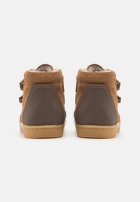 Stivali ankle in suede marrone con accenti marrone scuro, dotati di cinturini in velcro e suola in gomma. Il design presenta materiali testurizzati e colori a contrasto.