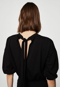 Vestido negro con un escote redondeado en la espalda, detalles anudados y mangas cortas abullonadas, confeccionado en una tela suave con un acabado mate.