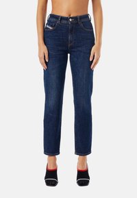 Blå denimjeans med rak bendesign, femficksstil, sömnadsdetaljer och metalldetaljer, i kombination med svarta och röda klackskor.