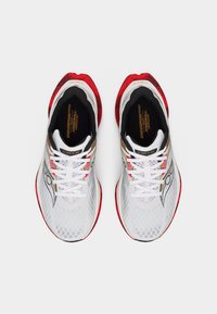 Ζευγάρι λευκών παπουτσιών για τρέξιμο με κόκκινες λεπτομέρειες, λευκά κορδόνια και μαύρο εσωτερικό, σε θέα από επάνω με απλό φόντο.