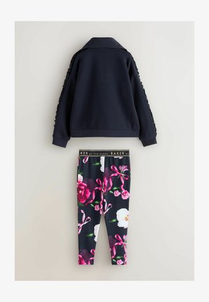 Jūras spēku flīsa jaka ar viļņainām plecu apdarēm, apvienota ar melnajām ziedu legingām, kurās ir rozā un baltas puķes un lentītes.