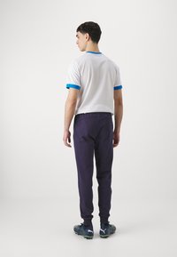Biely tričko s modrými akcentmi, kombinované s námorníckymi joggerm. Joggery majú užší strih a elastický pás. Športové topánky s akcentmi v zelenej farbe.