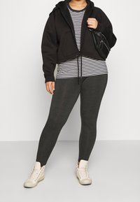 Sort cropped hoodie over en stribet skjorte, parret med mørke leggings og lyse høj-top sneakers. Glatte teksturer og minimal detaljering.