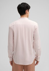Gemelli a manica lunga di colore rosa chiaro con strisce bianche, caratterizzati da un colletto rilassato e polsini abbottonati, realizzati in un morbido tessuto misto cotone.