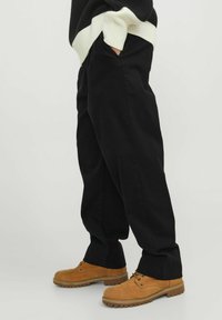 Pantaloni neri in cotone con tasche laterali, caratterizzati da una vestibilità ampia e gambe dritte, abbinati a scarpe in scamosciato color tan con dettagli stringati.