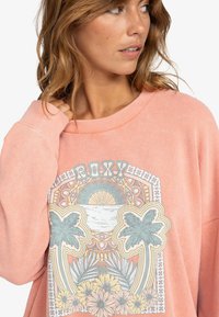 Helle rosa oversized Sweatshirt aus strukturiertem Stoff, mit einem bunten Grafikdruck von Palmen und floralen Details.