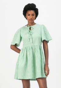 Vestido de mangas curtas em riscas verdes e brancas, com decote redondo e detalhe de amarração, apresentando uma saia rodada e um tecido leve e texturizado.