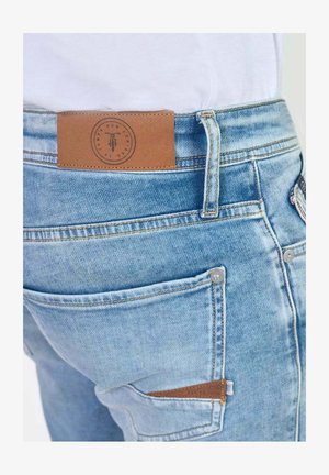 Light blue denim jeans with a brown leather patch on the waistband, featuring a contrast stitching and side pocket details.