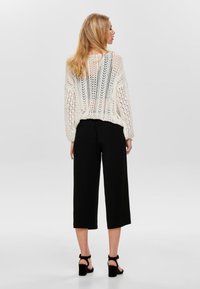 Hvit strikket genser med åpen vev og lange ermer, kombinert med svarte culottes og sandaler med høy hæl og stropper. Enkelt design.