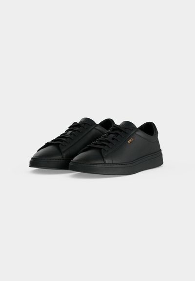 Paire de baskets basses noires à lacets avec dessus en cuir lisse et logo "BOSS" doré sur le côté.
