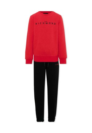 Felpa rossa a maniche lunghe con testo "John Richmond", abbinata a pantaloni neri con coulisse con piccolo logo rosso sulla coscia sinistra.