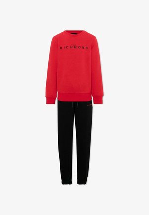 Sweat-shirt rouge à manches longues avec texte "John Richmond" associé à un pantalon noir à cordon avec un petit logo rouge sur la cuisse gauche.