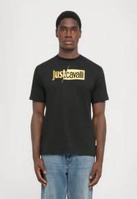 Juodos medvilnės marškinėliai su auksinės folijos "Just Cavalli" logotipu krūtinėje. Trumpomis rankovėmis ir klasikiniu apvaliu kaklu.