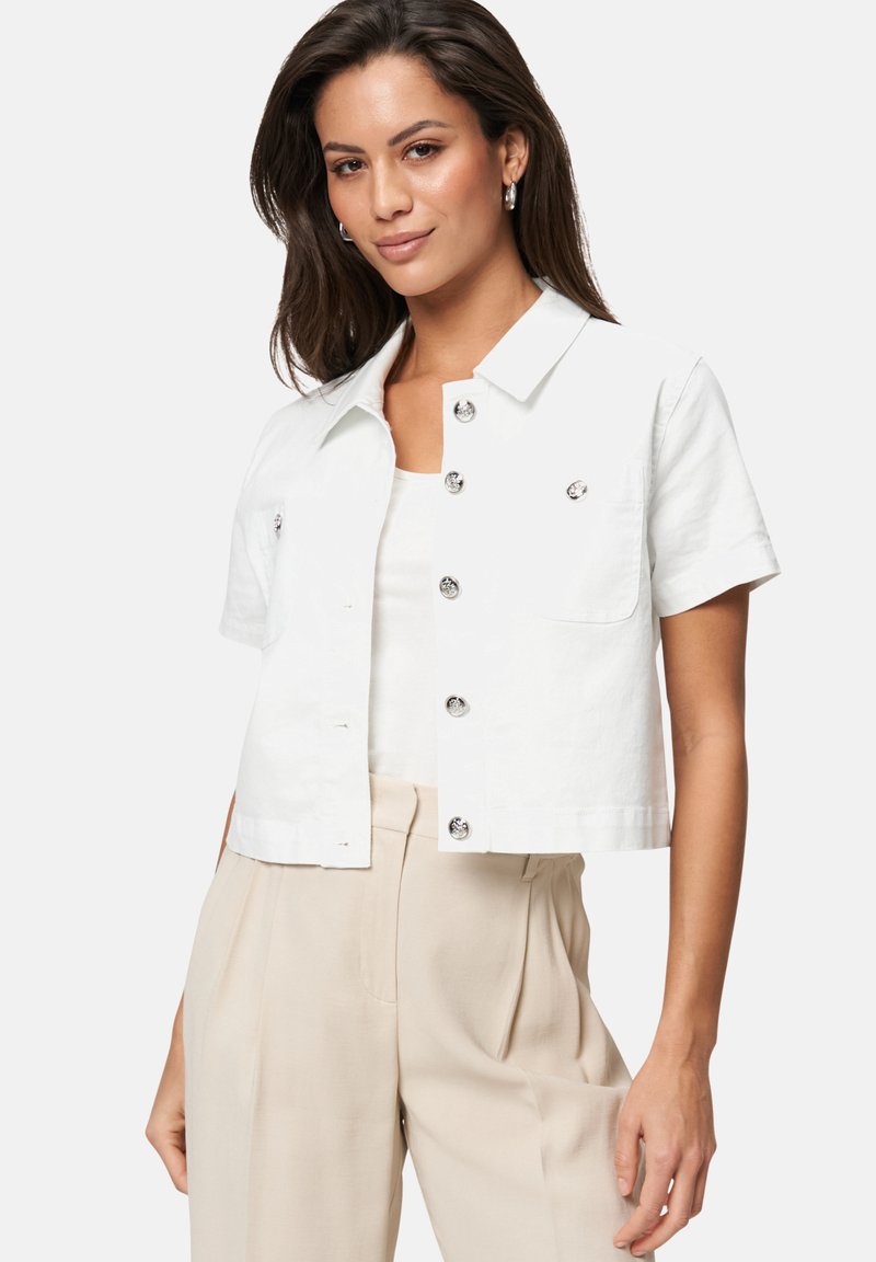 Witte cropped shirtjack, korte mouwen, knoopsluiting met metallic knopen, zakdetail, gecombineerd met beige broeken. Gladde stofstructuur.