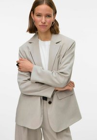 Vaaleanharmaa bleiseri, jossa on rento leikkaus, sakarat, yhden napin kiinnitys ja kaksi etutaskua. Yhdistetty valkoisen t-paidan kanssa.