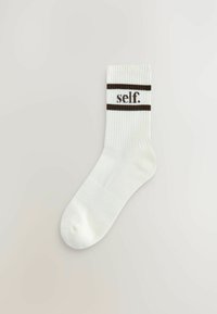 Bílé žebrované ponožky se dvěma hnědými vodorovnými pruhy nahoře a slovem "self." ve středu. Hladký materiál, délka do kotníku.
