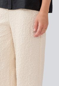Cream-colored trousers with a textured floral pattern, straight leg design, side seam pocket visible, paired with a black blouse.