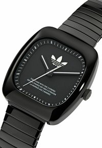 Must mustree kellaga käekell, millel on läikiv viimistlus, kolme triibuga logo, valged tunni markerid ja metallist link-riba. Disain on minimalistlik.