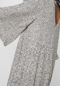 Musta-valkoinen kuvioitu mekko, jossa on lyhyet, liehuvat hihat ja matala selkäosa. Kangas on kevyt ja siinä on tekstuuri.