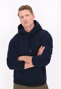 Námořnickě modrá mikina s kapucí vyrobená z měkké látky, s přední kapsou, žebrovanými manžetami a lemem, a s logem kotvy na hrudi.