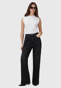 Schwarze hoch taillierte Jeans mit geradem Bein, seitlichen Schlitzen und einer glatten Textur. Kombiniert mit einem taillierten weißen ärmellosen Top.
