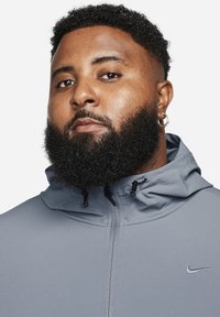 Nikei kapuutsiga jakk halli ühtlase tekstuuriga kangast, millel on reguleeritav kapuuts ja väike logo rinnal.