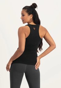Svart ärmlös träningslinne med en åtsittande design, med en orange logotyp på baksidan, ihop med mörka leggings.