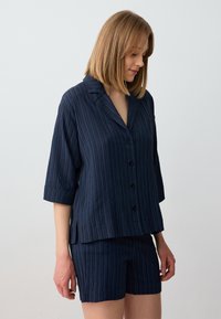 Set in blu navy con camicia a maniche corte caratterizzata da strisce verticali, chiusura con bottoni e pantaloni abbinati. Tessuto morbido e leggero con vestibilità comoda.
