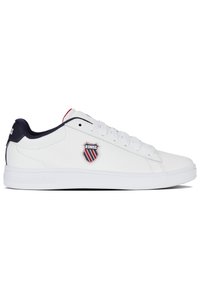 Baskets blanches avec un dessus en cuir lisse, accents marine au niveau du talon, et un patch logo rouge, blanc et bleu sur le côté. Semelle en caoutchouc.