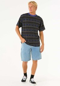 Kortærmet sort t-shirt med blå geometriske mønstre, kombineret med lyseblå denimshorts og sorte sneakers med hvide snørebånd.
