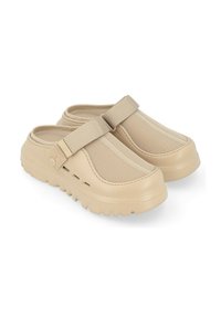 Zuecos beige sin cierres con suela de goma texturizada, parte superior de malla y correa ajustable. Cuenta con orificios de ventilación laterales para mayor transpirabilidad.