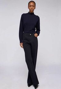 Černé široké kalhoty s vysokým pasem, hladkou texturou a minimálním zdobením, spojené s tmavě modrým dlouhým tričkem s rolákem.