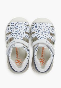 Sandalias blancas con patrones abstractos azules, diseño de punta abierta, múltiples correas, cierre ajustable de Velcro, plantillas acolchadas y suelas de goma.