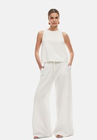 Vit, ärmlös crop top i kombination med högmidjade, vida byxor. Mjuk textur, minimalistisk design och sidfickor.