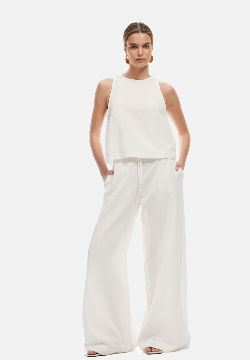 Vit, ärmlös crop top i kombination med högmidjade, vida byxor. Mjuk textur, minimalistisk design och sidfickor.