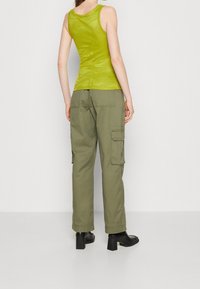 Débardeur vert côtelé à la coupe ajustée, associé à un pantalon cargo olive avec poches latérales, et des bottines noires à talons blocs.