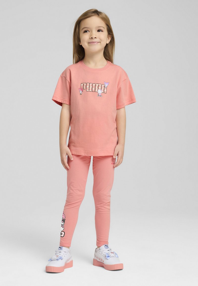 T-shirt in cotone rosa con un logo da cartone animato, abbinato a leggings coordinati. Presenta design grafici giocosi e sneaker bianche con suole rosa.