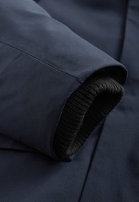 Gros plan d'une manche de veste bleu marine avec un poignet côtelé noir à l'intérieur de l'ouverture.
