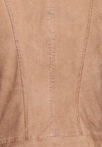 Helle sandfarbene, durchlochte Leder mit sichtbaren Nähten und strukturierten Oberflächen, die gleichmäßig verteilte Löcher für Belüftung und Details aufweist.