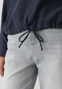 Top leggero blu navy con orlo regolabile, abbinato a jeans grigi chiari con una leggera texture e tasche.