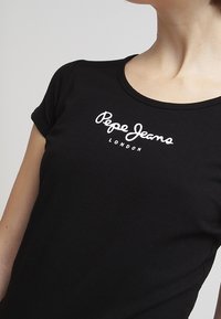 Camiseta de algodón negra con escote redondo y mangas cortas, que presenta el logo blanco de "Pepe Jeans London" en el frontal.