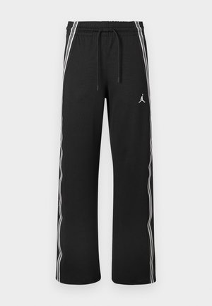 Pantalones deportivos negros con franjas blancas en los costados, cintura elástica con cordones y un pequeño logo Jumpman en el muslo derecho.