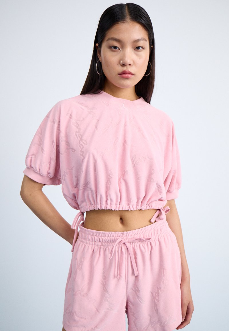 Felpa cropped rosa con maniche a sbuffo e orlo elasticizzato, caratterizzata da un sottile motivo script, abbinata a pantaloni corti con cordoncino nello stesso colore.