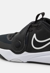 Svarta Nike-sneakers med texturerad ovandel och en vit swoosh, utrustad med snörning och ett band för en säker passform mot en vit bakgrund.
